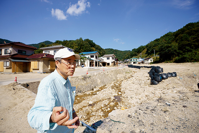 吉川三郎（よしかわ・さぶろう）さん│71歳│広島県坂町（さかちょう） 「普段は水量も少なく穏やかな天地川が氾濫し、住宅が流されました。ここにも、アパートや家屋が建っていたんですよ」と語る吉川さん 取材／多田茂樹　写真／堀 隆弘