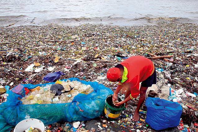フィリピンのマニラ湾に打ち上げられたごみの中からプラスチックのカップを集める人。2016年8月(ロイター=共同)。このように、世界の海岸には膨大な量のプラスチックごみが打ち寄せられている
