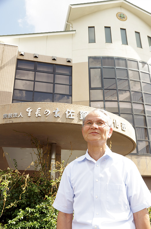 山本英夫(やまもと・ひでお)さん│71歳│佐賀県基山町 通い慣れた生長の家佐賀県教化部の正面玄関の前に立ち、晴れ晴れとした笑顔を見せる山本さん 取材/多田茂樹 写真/近藤陽介
