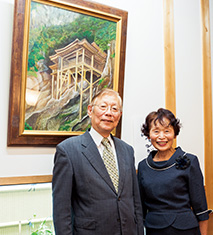 妻の紀代子さんと倉吉市内の自宅で。後ろの作品は、鳥取県の名所、投入堂を描いたもの