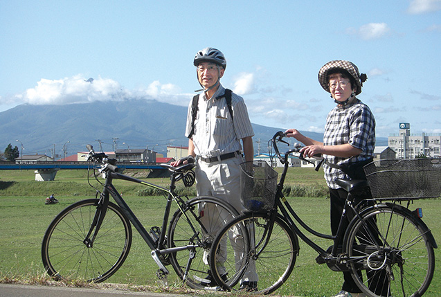 小田川浩三（おだがわ・こうぞう）さん 69歳 青森県五所川原市 妻の多加代さんと共にポタリングし、居住地の豊かな自然に触れ、喜びを分かち合う。岩木山を背に岩木川の土手で 取材／原口真吾（本誌）　写真提供／小田川浩三さん