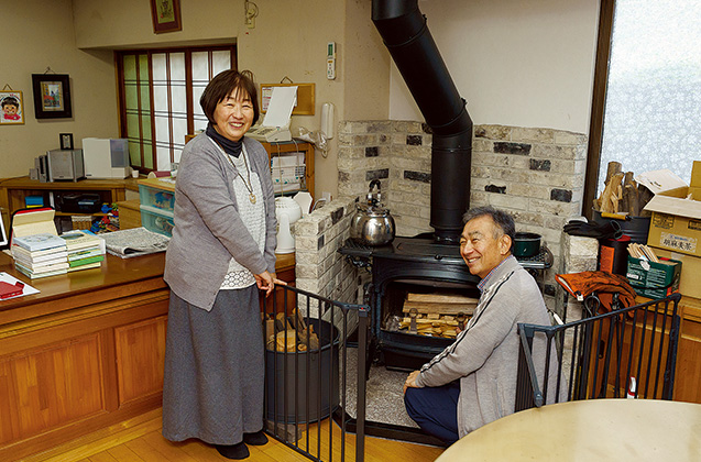 夫の金良（かねよし）さんと薪ストーブの置かれた自宅で