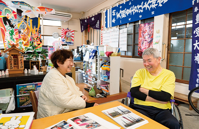 自宅でもある紫谷染物店で、スクラップブックを開いて思い出話に花を咲かせる。店にはさまざまな染物のサンプルが所狭しと並び、最近は、五月幟を法被にリメイクする注文もあるという（写真／髙木あゆみ）
