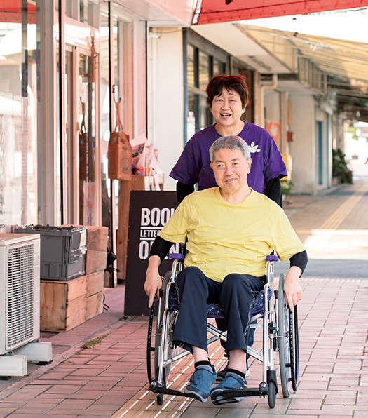 商店街で車椅子をこぐ英幸さんに、ゆかりさんが後ろからそっと手を添える（写真／髙木あゆみ）
